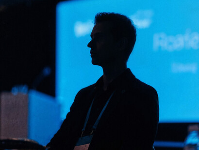 The silhouette of a man seated at a conference, focused on the speaker
