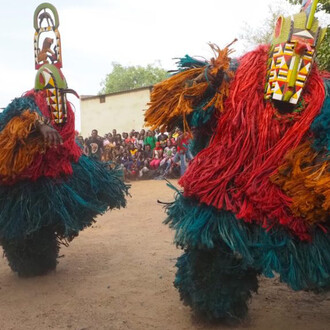 Headpiece carved by David Sanou in the studio of André Sanou, A pair of Kimi masks performing greetings with the lead griot Tchiedo playing his drum behind them, Bindougosso district, Bobo-Dioulasso, Burkina Faso, May 3, 2022. Courtesy of NOMA