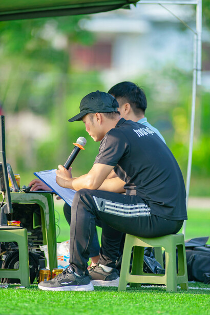 On the sports field, a man uses a portable computer while the football manager and director of football discuss strategy