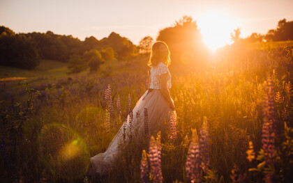 A woman in a bright dress walks across a field in the glow of sunset