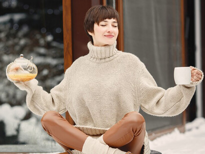 In a white sweater, a woman savors a cup of tea, embracing the tranquil beauty of nature during the winter season