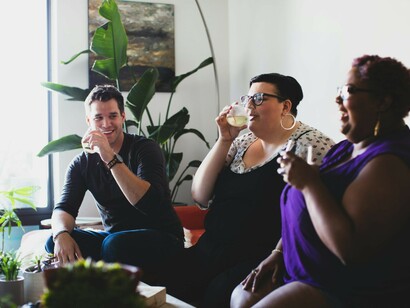 A smiling man and two overweight women are enjoying drinks together in the living room