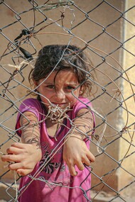 A young girl grips a chain-link fence in Idlib, Idlib Governorate, Syria