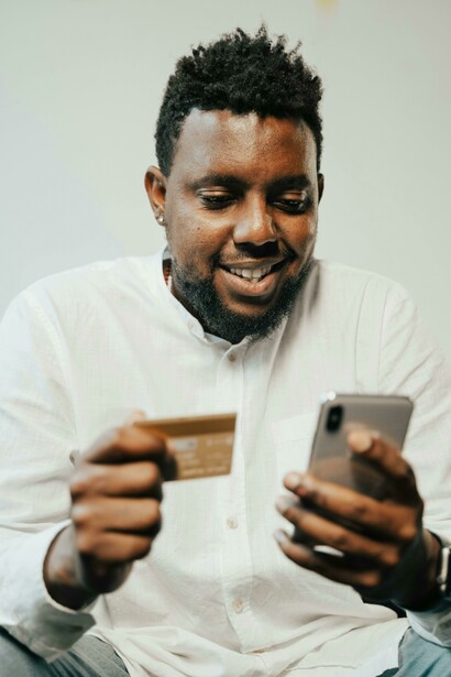 A man wearing a white long-sleeved shirt holds a cellphone and a card as he reads shocking news in an email