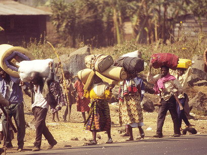 A stream of Rwandan refugees, carrying all their possessions, walks into Goma after civil war erupts in their country. They join over 1.2 million other refugees in overcrowded camps, where a cholera outbreak claims an estimated 2,000 lives daily