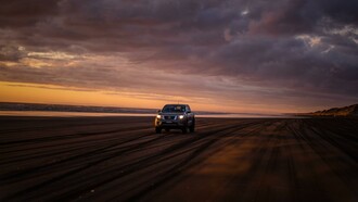 A car driving alone on a beach at sunset