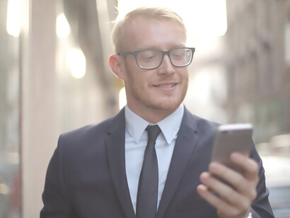 A suited man, strolling down the street, beams with joy as he receives positive news over the phone