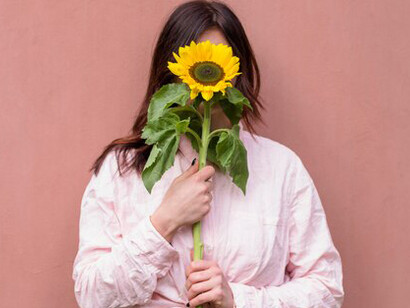 With a fresh yellow flower held close to her face, a woman expresses self-love, authenticity, personal growth, and celebrates the freedom to be unique and the courage to fail