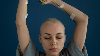 A shaved young woman with eyes closed and arms reaching up