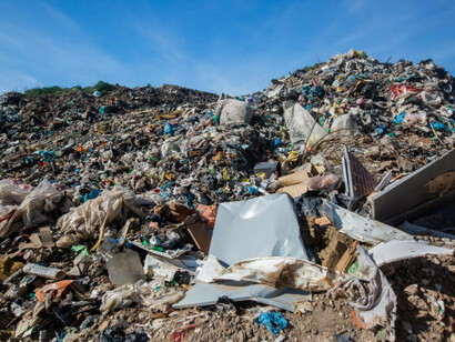 A vast landfill overflowing with trash and plastic debris stands in stark contrast to the bright blue sky, underscoring the urgent challenges of waste management and environmental pollution