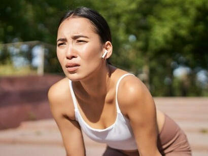 A fatigued young woman runner stops jogging to catch her breath, struggling with pressure