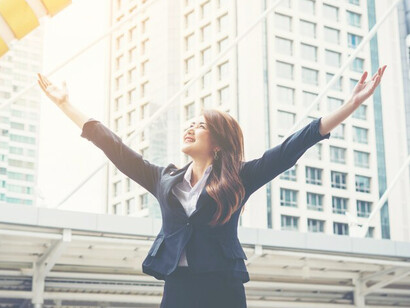 A successful businesswoman, dressed in a dark suit, joyfully raises her hands while overlooking the city center, symbolizing career development and professional success