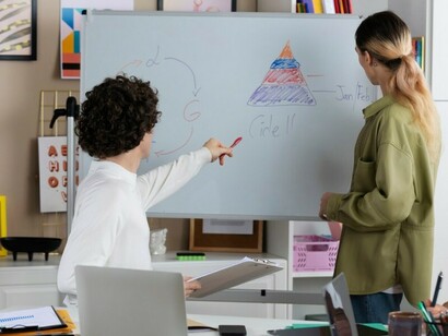 Students are gathered around a whiteboard, actively discussing and collaborating on their ideas