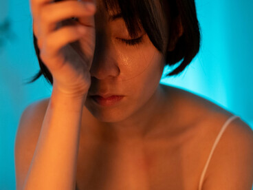A short-haired woman in a white tank top holds her face in distress