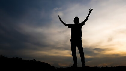 A strong human figure with his hands stretched towards the sky