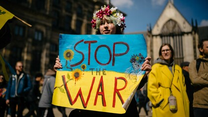 A fotografia de Michael Mücke mostra uma mulher com uma coroa de flores na cabeça, maquiagem que simula sangue no rosto e uma faixa com a mensagem “Stop the War” (“Parem a guerra”). A imagem combina a força visual do protesto com a expressão individual de quem transforma a indignação em manifestação pública. Embora a fotografia não tenha sido feita na Ucrânia, ela dialoga com a dimensão internacional do conflito e com a necessidade de colocar a proteção da vida acima dos interesses militares e geopolíticos