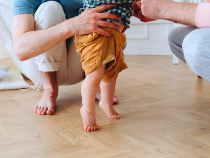 Pai e sogro seguram bebê que tenta se manter em pé