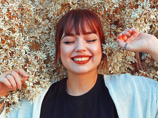 A woman in a black crew-neck top and white cardigan lies among the daisies