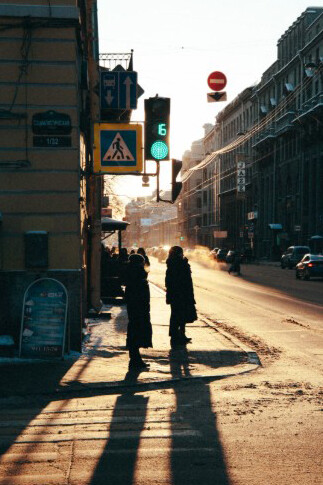 As the sun sets over Saint Petersburg, people pause at a crossroads, casting long shadows on the quiet sidewalk, Russia 