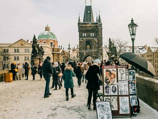 Tourists exploring Charles Bridge, Prague, beside a caricature artist’s display, symbolising the city’s beautiful cultural character