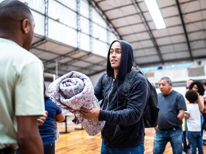 A young man receiving a blanket from a volunteer at a shelter