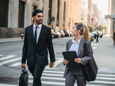 A professionally dressed couple walking side by side through the city, representing the journey of pursuing success together
