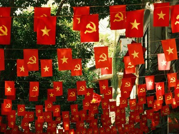 Faixas e bandeiras com referências ao comunismo ocupam o cenário de uma rua arborizada de uma cidade. O texto utiliza o tema para discutir valores, disputas ideológicas e a percepção do autor sobre o momento político contemporâneo