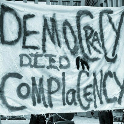 Manifestante en Estados Unidos, sosteniendo un cartel que dice: "La democracia murió en la complacencia"