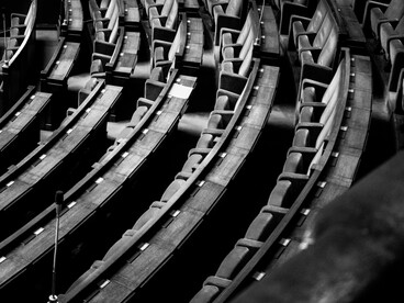 Toma en blanco y negro en ángulo picado que muestra la disposición curva e inclinada de las filas de asientos vacíos en un auditorio o parlamento