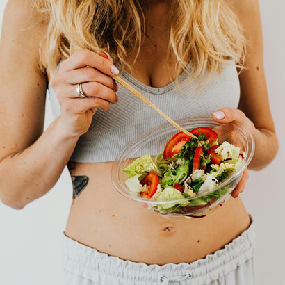 A fit woman enjoys a fresh vegetable salad while tracking her calorie intake and maintaining healthy eating habits