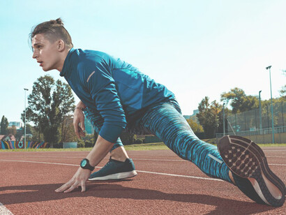A male athlete is warming up by stretching his legs before a training session on the stadium tracks, optimizing his preparation for peak performance