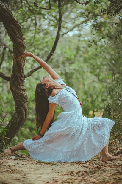 A woman crouched close to the earth while raising her hands upward in a moment of reflection and connection