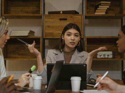 A woman in a gray blazer presents a report during a board meeting, contributing ideas in a business brainstorming session
