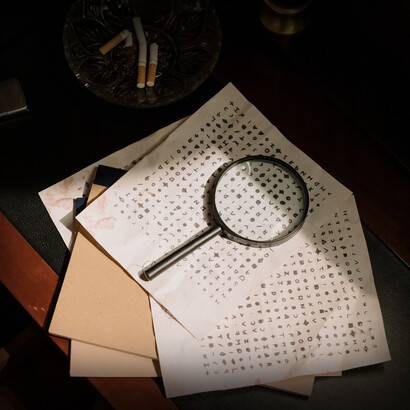 Lupa e manuscritos sob a mesa de um investigador compõem a cena de uma gravação