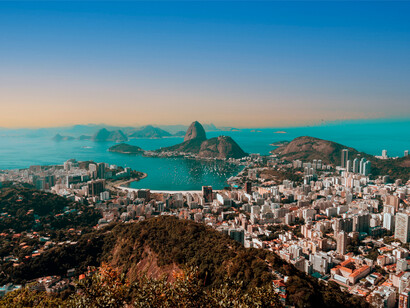Cidade do Rio de Janeiro, Brasil. Quando a cidade desperta, há sinais, não há um despertador exato, mas há sons que se destacam, buzinadelas, motores a arrancar, persianas que levantam, máquinas de café que se multiplicam e se ligam, cadeiras que arrastam e sapatos e sapatilhas que andam a passo apressado