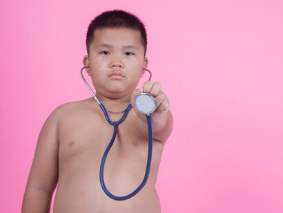 A young boy with obesity poses in front of a pink backdrop, highlighting the issue of childhood overweight
