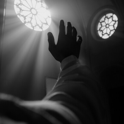Una mano extendida hacia arriba alcanzando la luz solar que atraviesa el rosetón de una iglesia