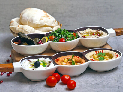 A selection featuring different types of hummus, seasoned vine leaves and salads
