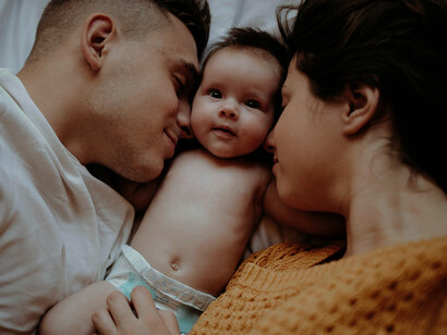 Parents and their baby share a playful moment on a bed, highlighting the warmth, affection, and joy of family life