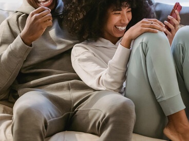 A happy Black couple sits together on a couch, enjoying a vertical microdrama on their smartphone