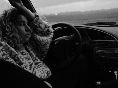 A figure clad in a subdued gray and white sweater sits behind the wheel of a car