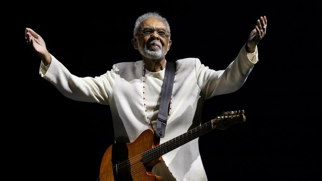Gilberto Gil no palco, durante a turnê Tempo Rei, no Mineirão, em 2025, com os braços abertos, a guitarra presa ao corpo e um fundo completamente escuro. De braços abertos diante do público, o artista parece acolher as muitas histórias e gerações que sua música acompanhou ao longo de mais de seis décadas de carreira. Do primeiro LP Realce ouvido aos 10 anos ao show de despedida dos grandes palcos, sua música atravessou décadas e se misturou às memórias de uma vida. Sob a luz do palco, a imagem parece traduzir o próprio espírito da canção: o tempo passa, transforma as formas do viver e, ainda assim, algumas músicas permanecem