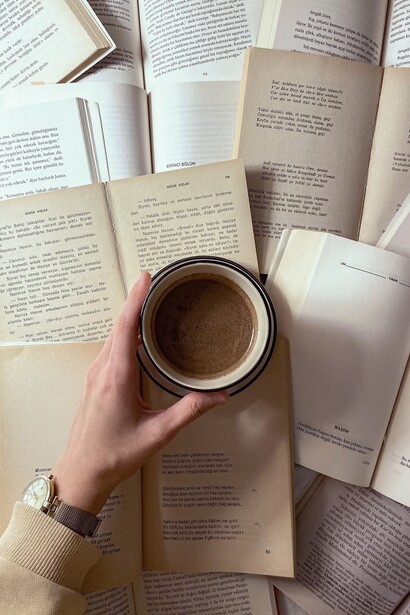 A woman's hand holding a cup of coffee, while reading a bunch of open books, all at the same time, human curiosity has no ending and no limits