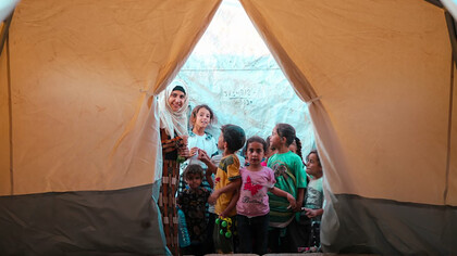 Displaced by conflict in the Middle East, a group of refugees gathers inside a tent