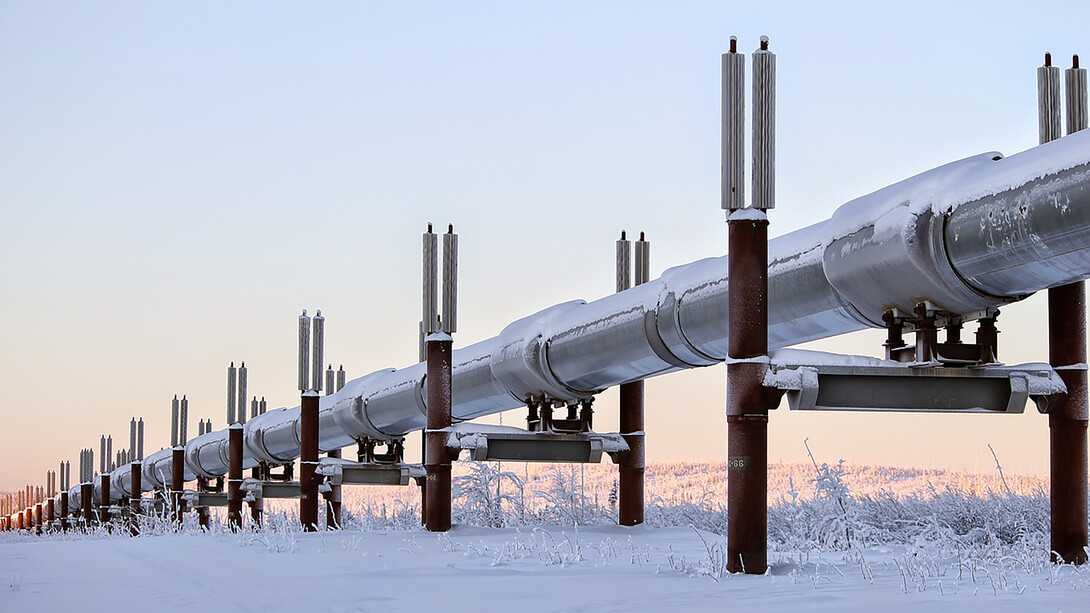 A snow-covered oil pipeline stretches across the Alaskan winter landscape