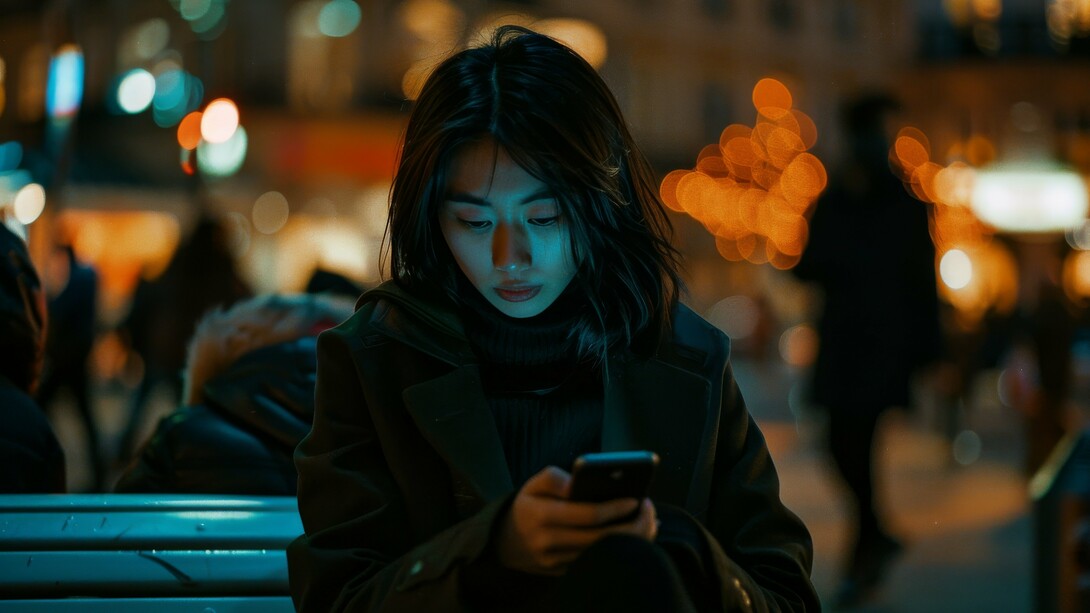A girl sitting outside at night, her attention captured by her phone, illustrating how algorithms train the brain toward constant novelty