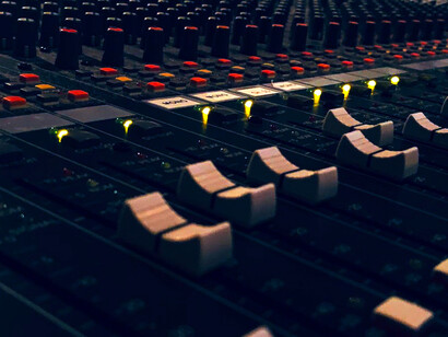 A complex analog sound board covered in knobs contrasts with a digital interface showcasing an AI-generated song, highlighting the fusion of human and machine-made music