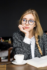 A cheerful woman sits in a cozy café, engrossed in a book, radiating warmth and joy as she enjoys her peaceful moment surrounded by the inviting ambiance