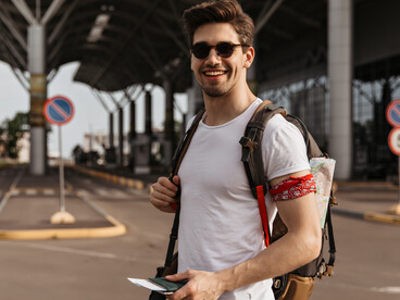 A solo traveler in a white T-shirt and sunglasses smiling near an airport