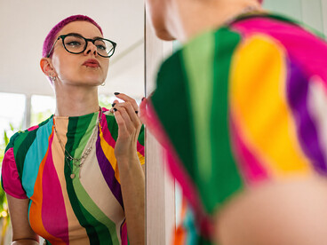 Young woman with short pink hair applying lip gloss while looking into a mirror